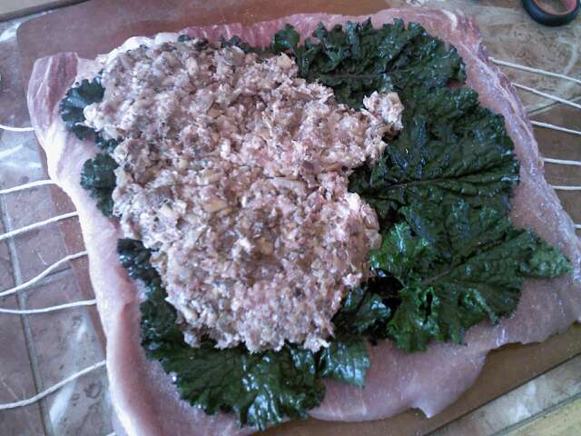 Butterflied pork loin covered with kale and stuffing and ready to roll up.